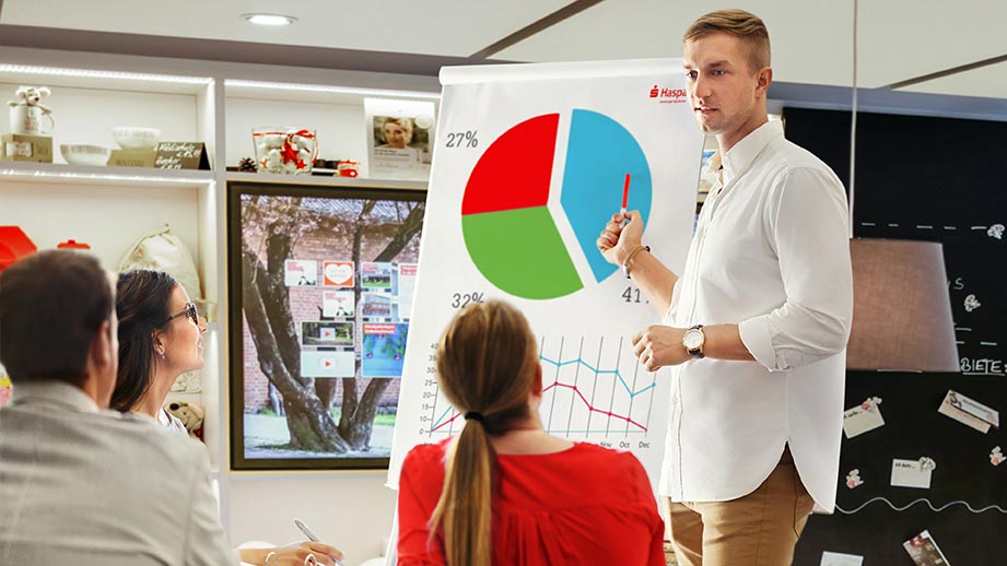 Ein Mann steht vor einer Gruppe von Personen und präsentiert ein Diagramm auf einem Flipchart.